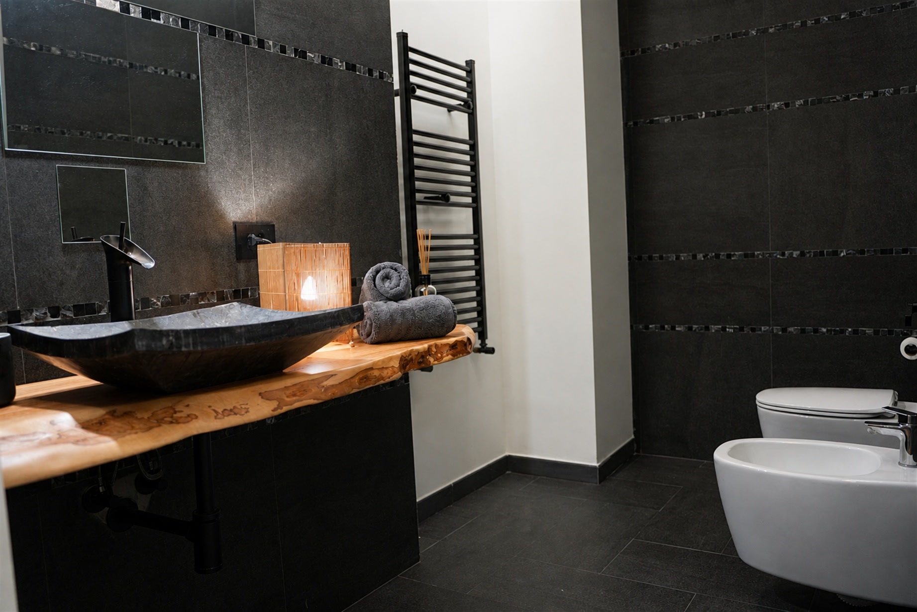 Bagno con lavabo in pietra su mensola di legno vivo e parete scura