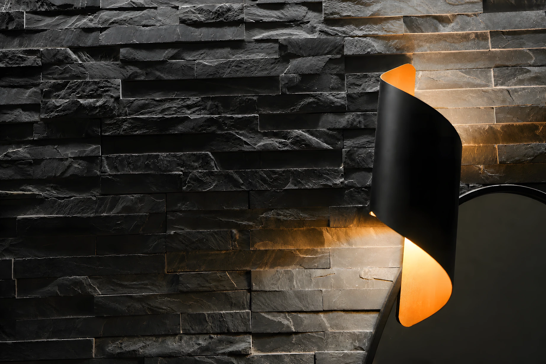 Parete in pietra lavica nera illuminata da un'applique nera e oro