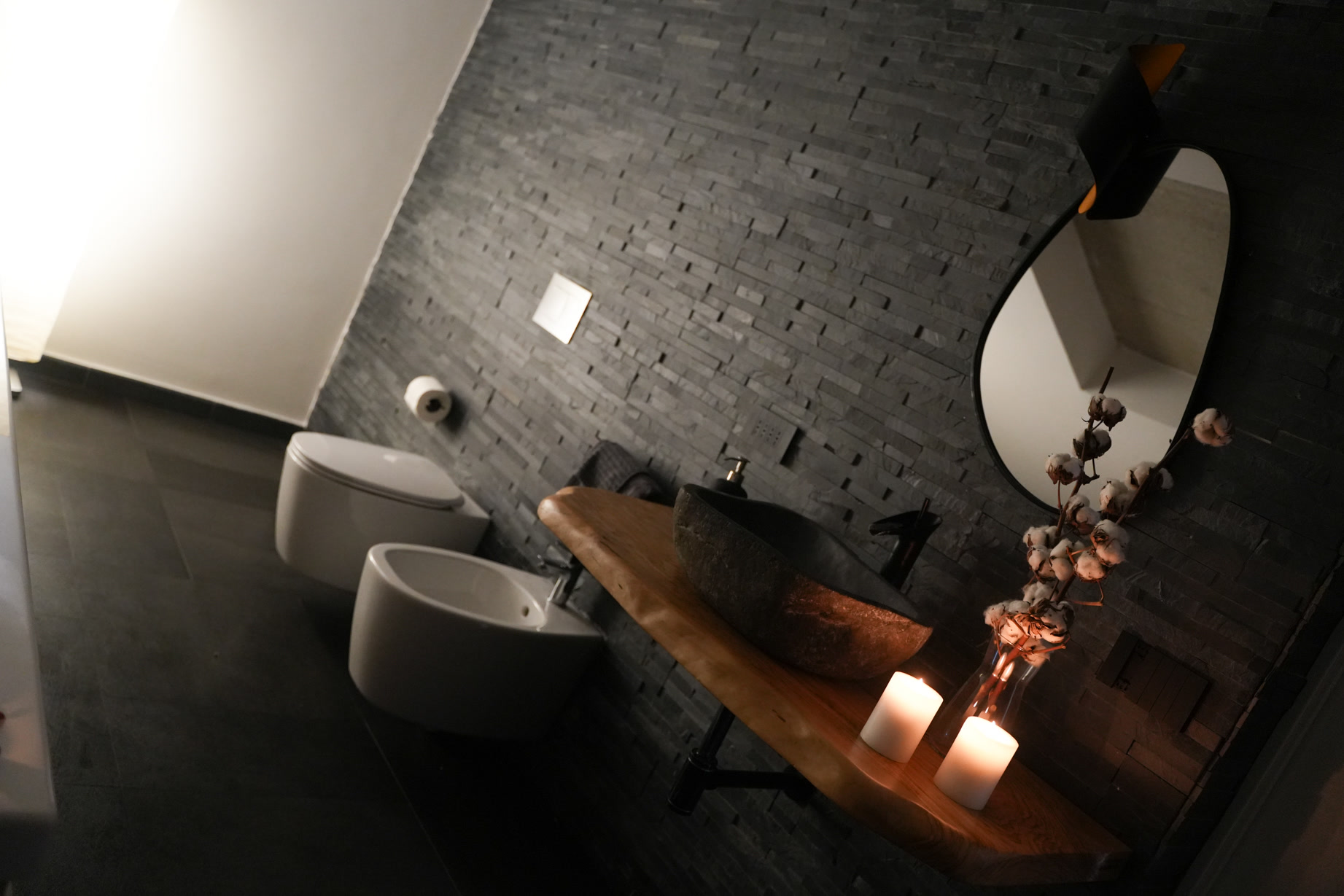 Il bagno della suite: lavabo in pietra su mensola di legno massello, specchio sagomato e parete in pietra nera
