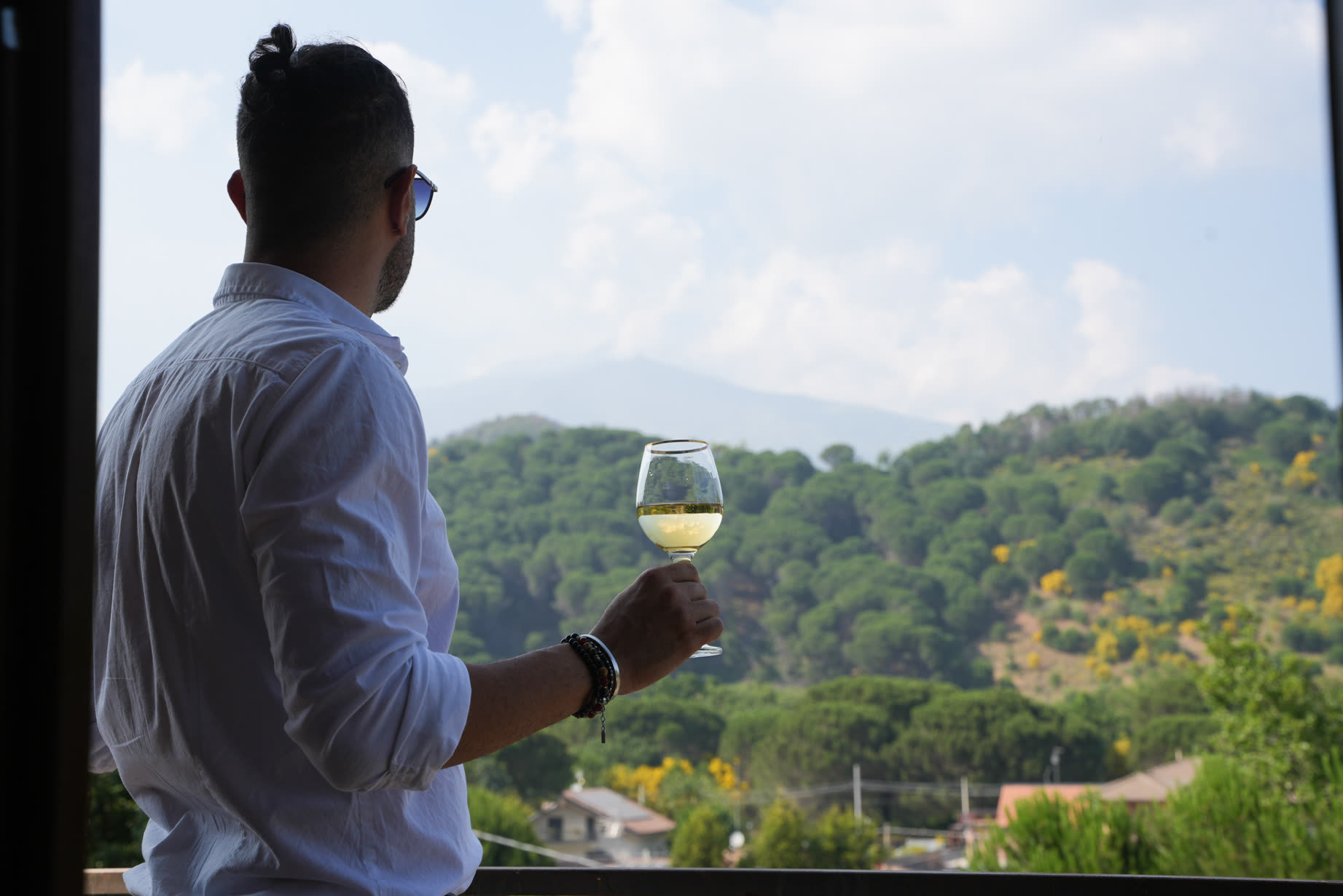 Ospite di spalle al balcone con un calice di vino bianco, davanti alle colline verdi