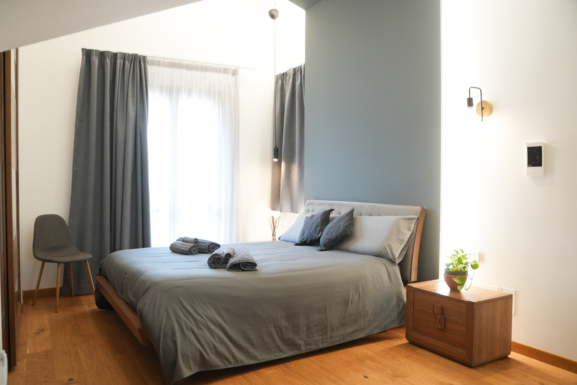 Camera della suite Theros: letto con testiera imbottita, legno e tende grigie, luce naturale morbida