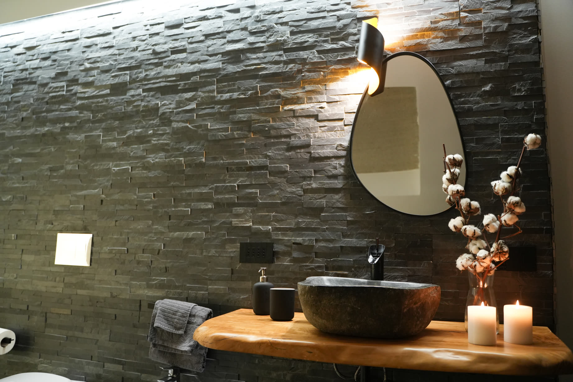 Lavabo in pietra con fiori di cotone e candele contro il muro lavico