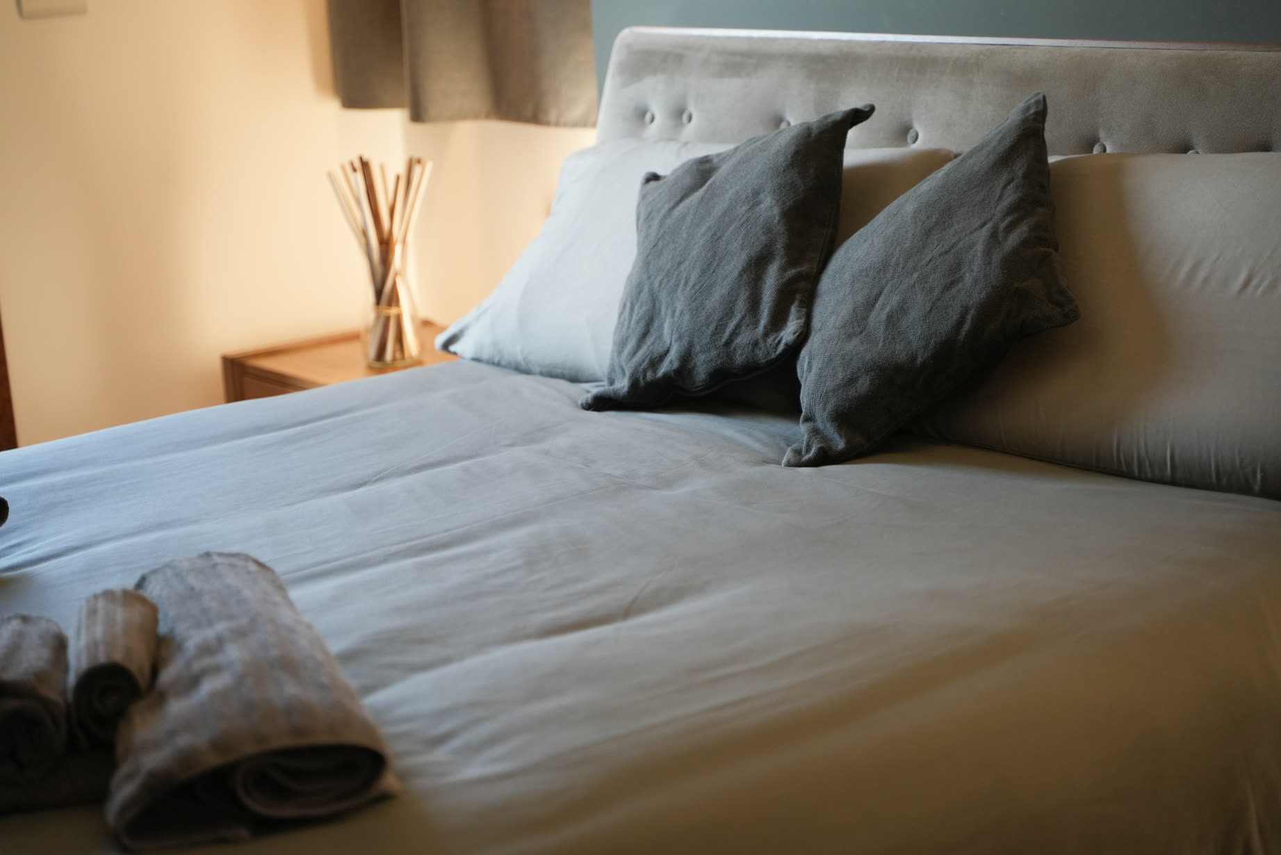 Letto rifatto con cuscini grigi nella suite Tifone, luce laterale calda