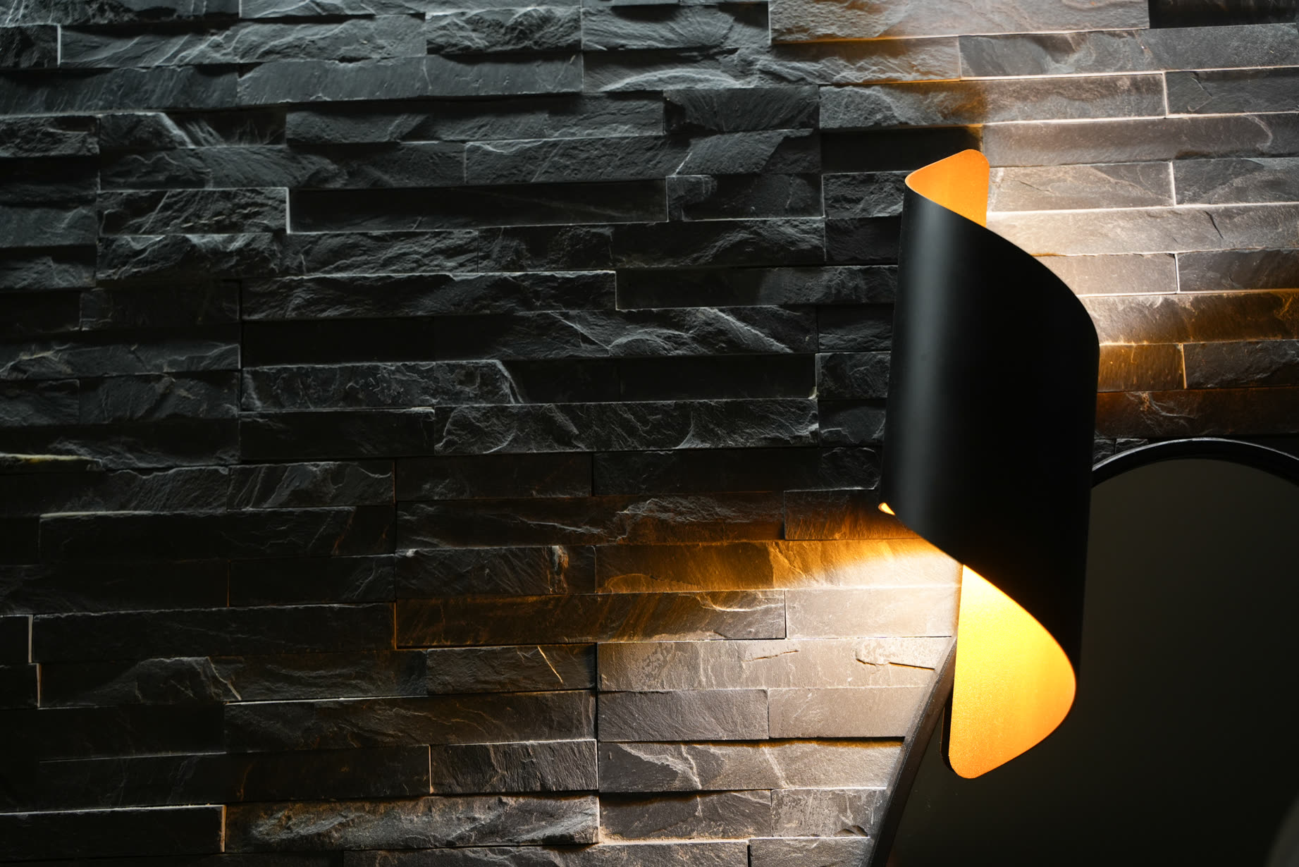 Parete in pietra lavica nera con applique in nero e oro accesa, nella penombra