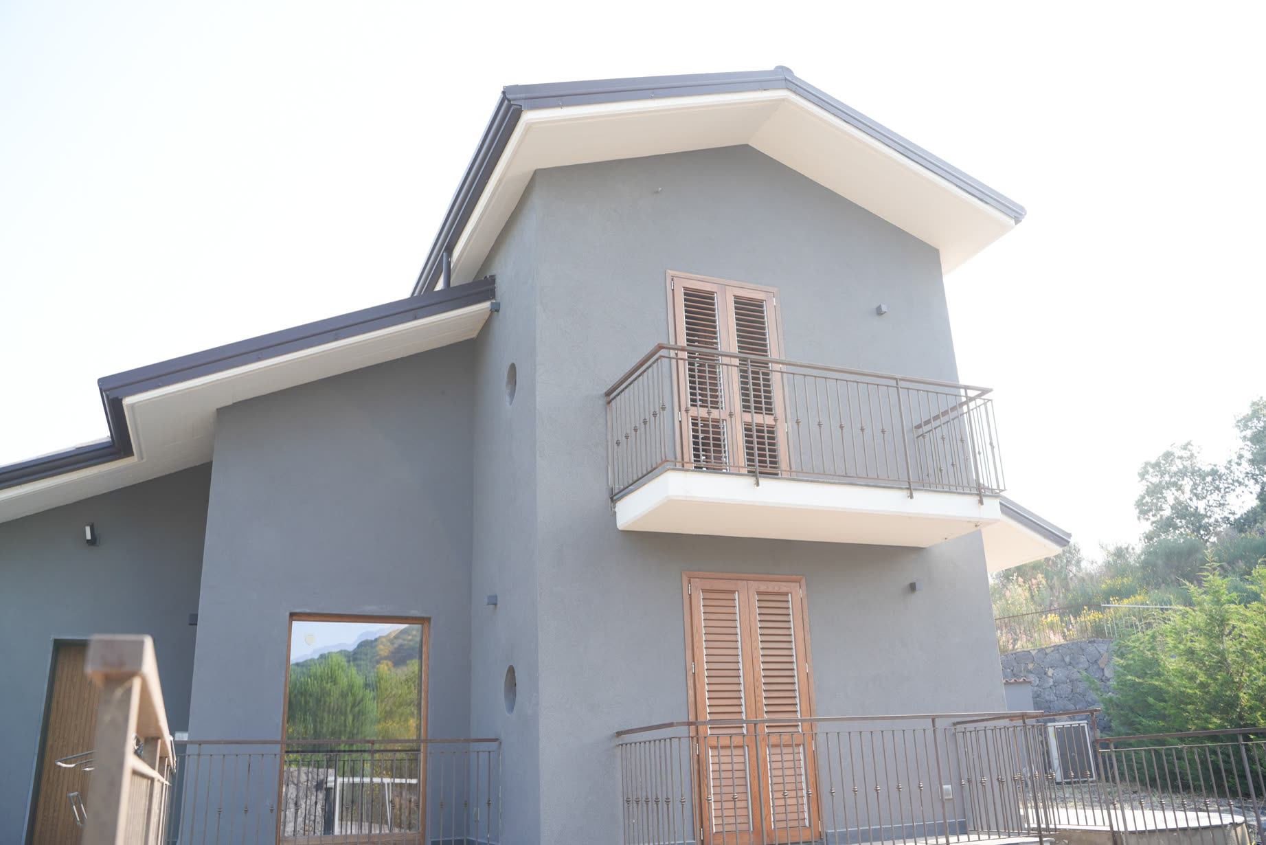 Esterno della villa: architettura contemporanea grigia con infissi in legno e finestra a oblò